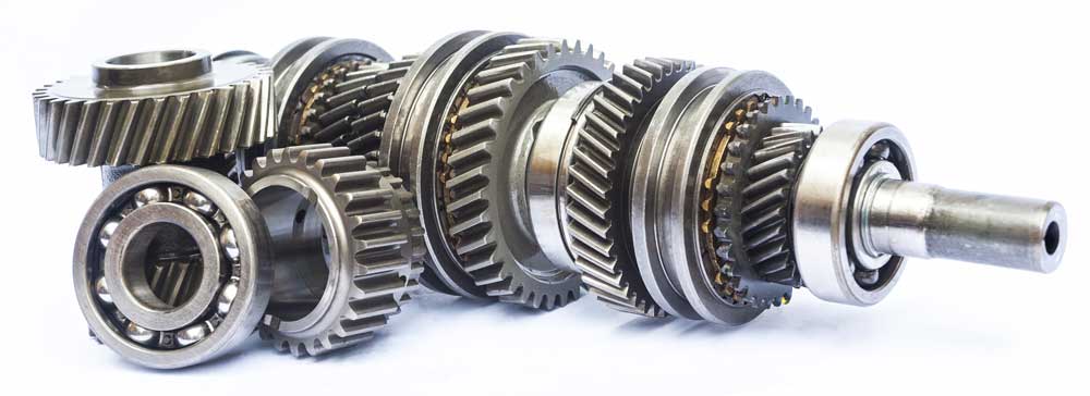 Close-up of a gear shaft assembly with multiple interlocking metal gears and bearings arranged along a central shaft, showing detailed machining and varying gear sizes.