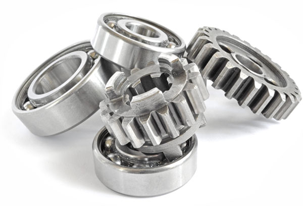 Close-up of several metal machine components, including ball bearings and toothed gears, arranged together with a polished steel finish on a light background.
