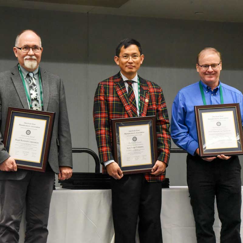 Three men standing side by side holding framed certificates, dressed in business attire, posing at an indoor awards or recognition event.